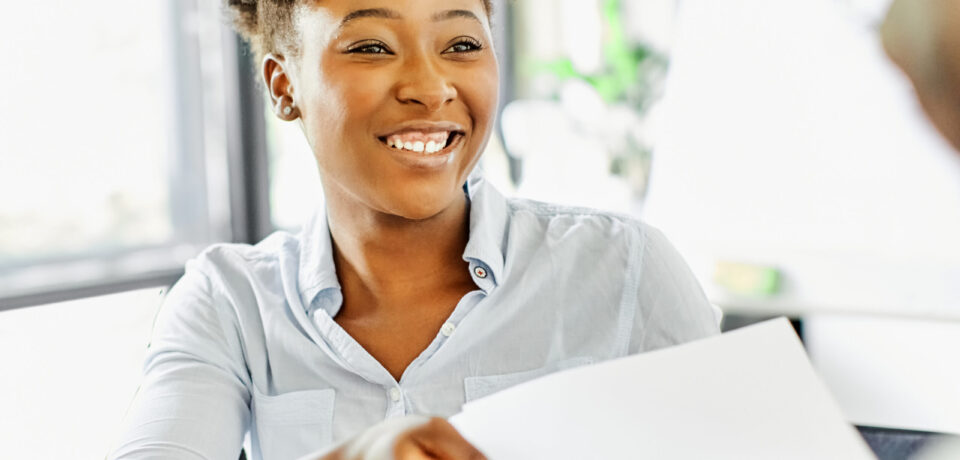 portrait of a smiling young businesswoman doing paperwork and passing document or a contract in the office